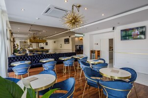 Een modern restaurantinterieur met blauwe velours zitplaatsen, ronde tafels en een unieke goudkleurige sterrenbloem kroonluchter.