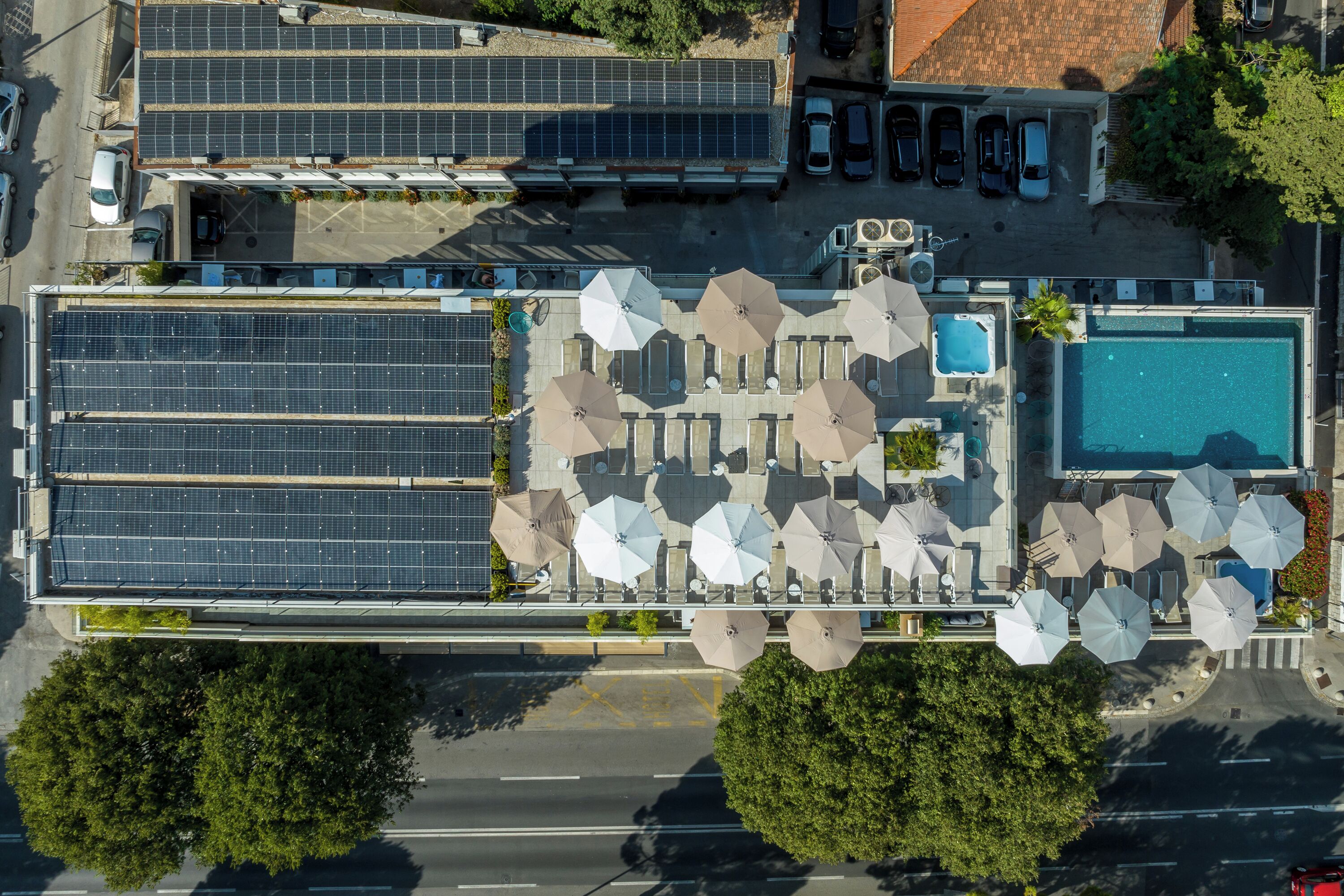 Luchtfoto van een hotel met zonnepanelen, terras, zwembad en parkeerplaats.
