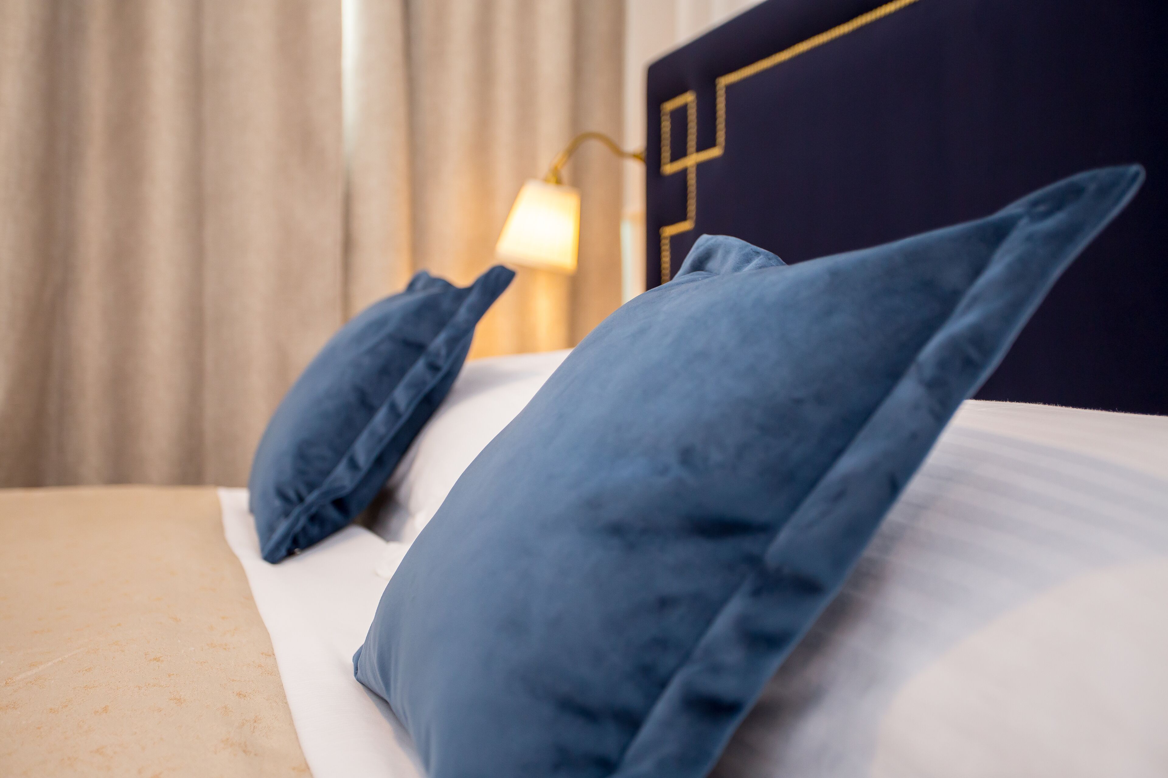 A bed with blue pillows and a white mattress, a lamp on a bedside table, and a dark headboard with a geometric design.