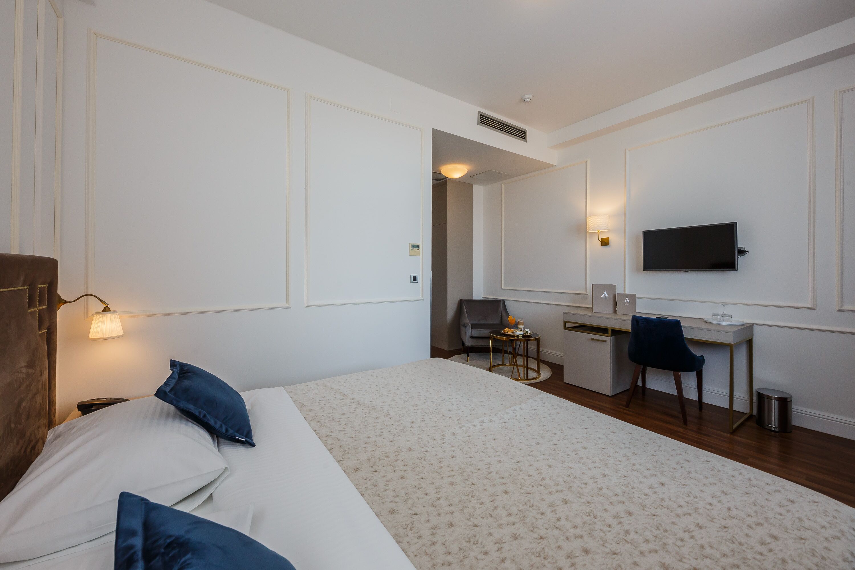 Ein Hotelzimmer mit Bett, Schreibtisch, Stuhl, Fernseher und einem kleinen Tisch mit Lampe.