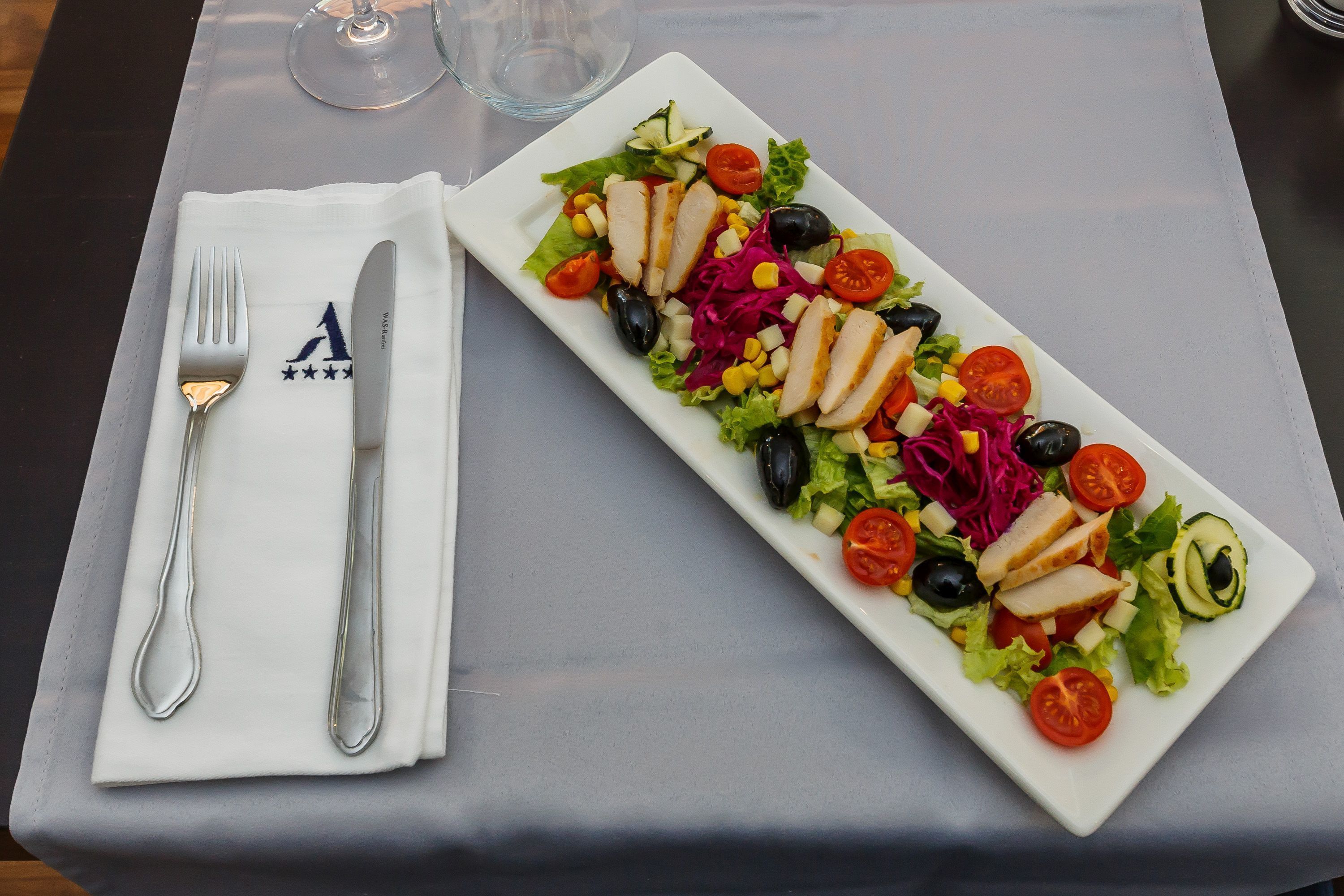 A rectangular white plate with a colorful salad, a fork, and a knife on a table.