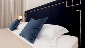 A neatly made bed with white linens and two blue pillows, a dark headboard with a geometric gold design, and a lamp on the nightstand.