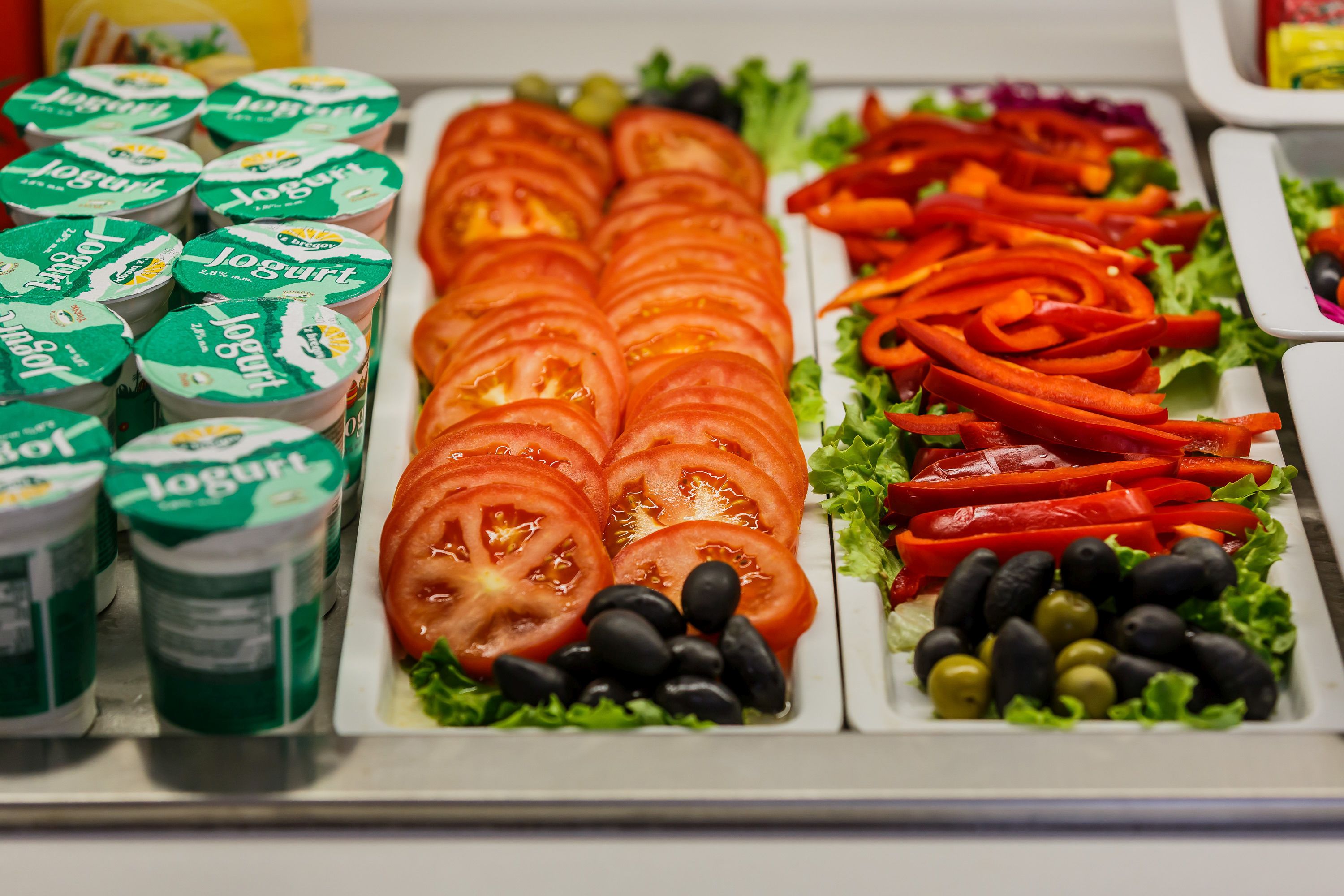 Una barra de ensaladas con diversas verduras frescas y recipientes de yogur.