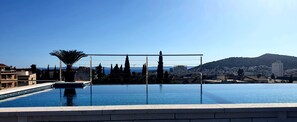 A rooftop infinity pool with a clear view of the city and mountains in the background.