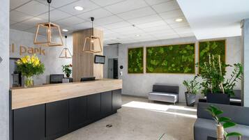 A modern reception area with a wooden reception desk, black cabinets, and pendant lighting. There are two large green moss wall art pieces and several potted plants.