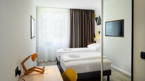 Une chambre d’hôtel comprenant un lit, un bureau avec une chaise, un téléviseur fixé au mur et une fenêtre avec des rideaux.