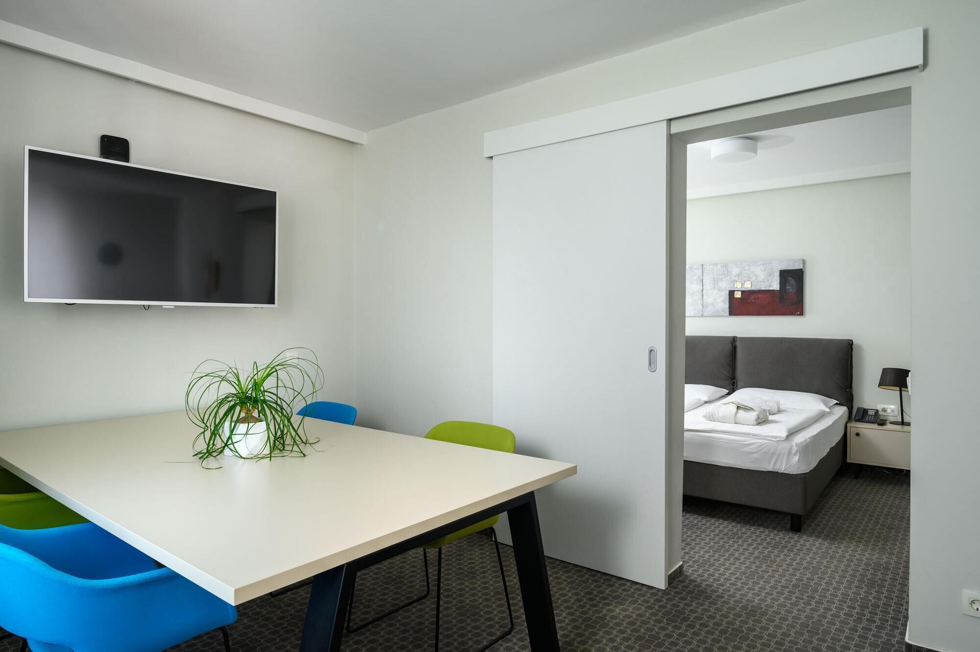 A hotel room with a bed, bedside table, lamp, and a TV mounted on the wall.