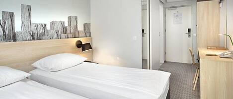 Habitación de hotel con dos camas, cabecero de madera, lámpara de pared, escritorio con silla y puerta que da a otra habitación.