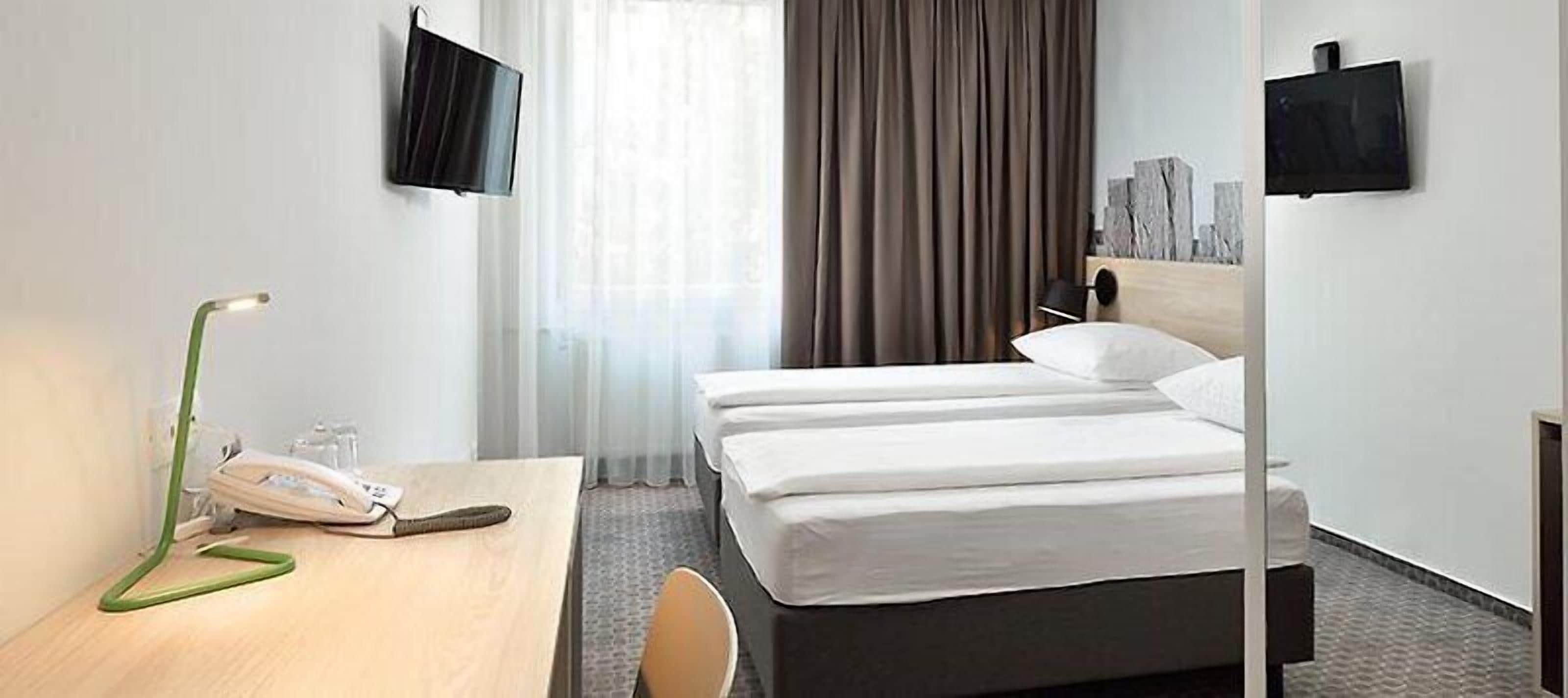 Habitación de hotel con dos camas, un escritorio con teléfono y dos televisores instalados en la pared.