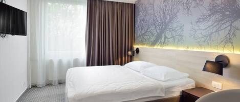 A hotel room with a bed, a nightstand, a wall-mounted TV, and a window with curtains.