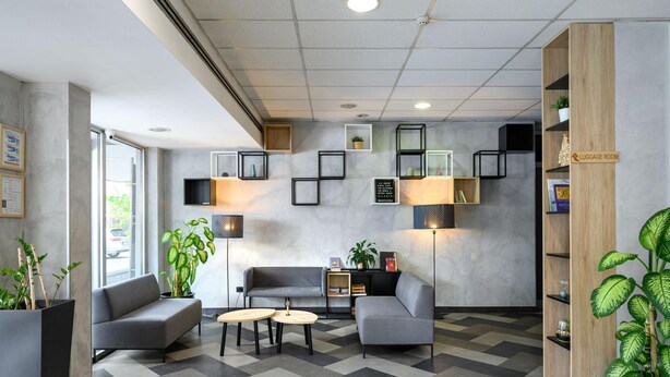 Un hall d’entrée moderne avec des canapés gris, une table basse et un panneau indiquant l’emplacement de la consigne à bagages.