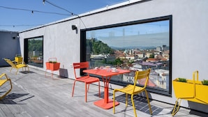 Une terrasse sur le toit avec une table et des chaises, une grande fenêtre donnant sur la ville et un éclairage extérieur.