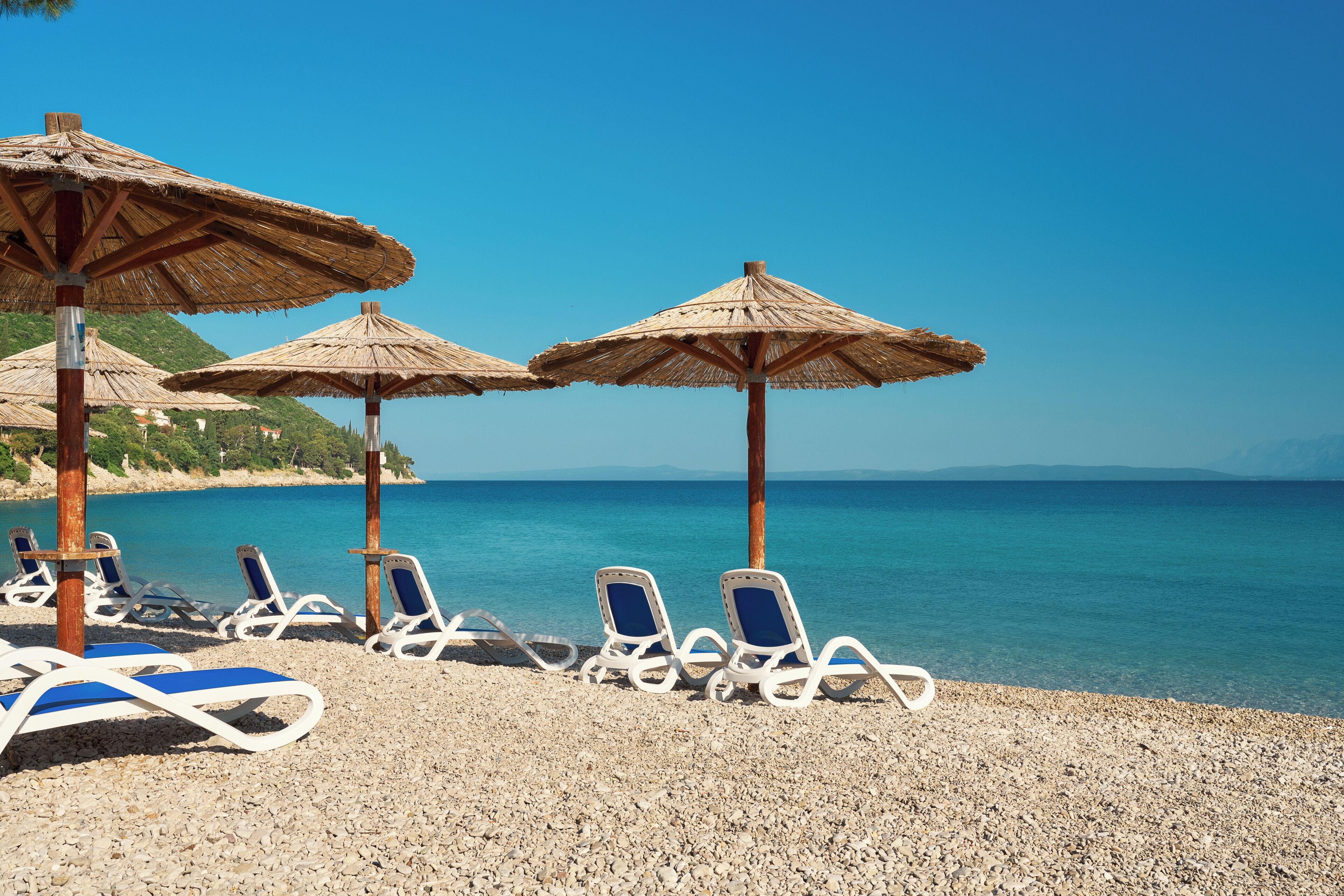 A beach with lounge chairs and thatched umbrellas.