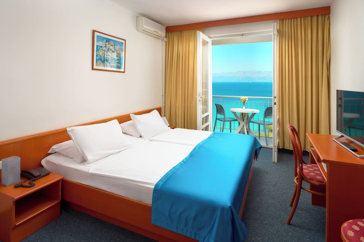 Quarto de hotel com cama, escrivaninha com cadeira, mesa pequena com cadeira e varanda com vista para o mar.