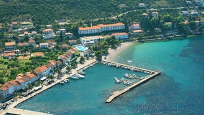 Vista aérea de un pueblo costero con un puerto deportivo, edificios residenciales y un gran hotel con techo rojo.