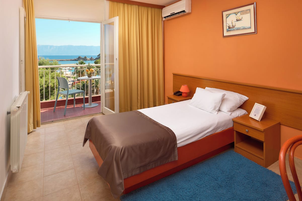 Quarto de hotel com cama, mesa de cabeceira, cadeira, vista para o mar e varanda.