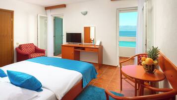 A hotel room with a bed, a desk, a chair, a television, and a view of the sea.