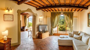 Un salon chaleureux avec un plafond en bois, une télévision, un canapé et une vue sur la verdure à l’extérieur.