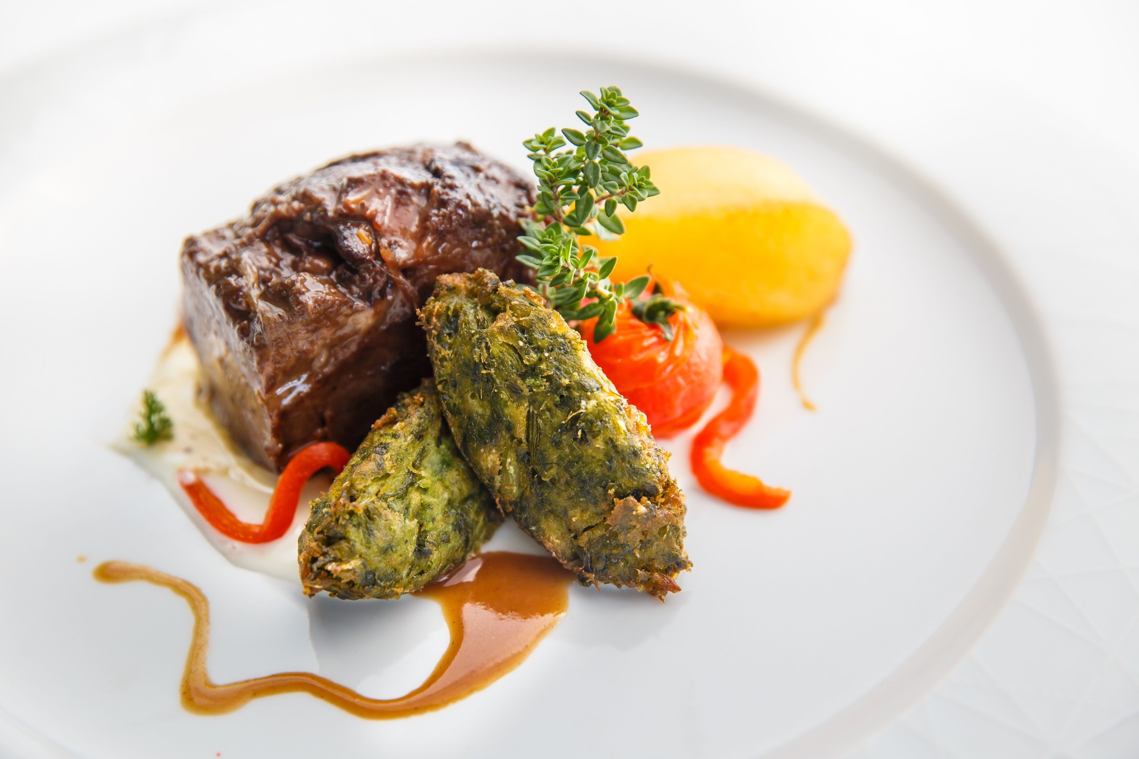 A plate with a piece of meat, a green vegetable, a red vegetable, and a yellow item, all arranged on a white plate.