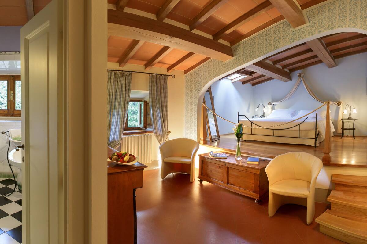 Un dormitorio con techo de madera, una cama, una mesita de noche y un ventanal con cortinas.
