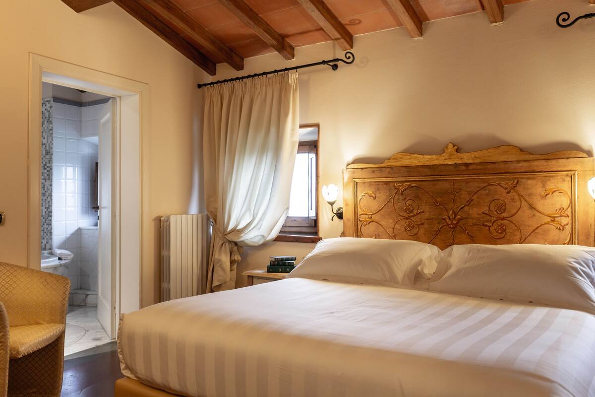 Une chambre à coucher comprenant un lit, une chaise, une table de chevet et donnant sur une salle de bain.