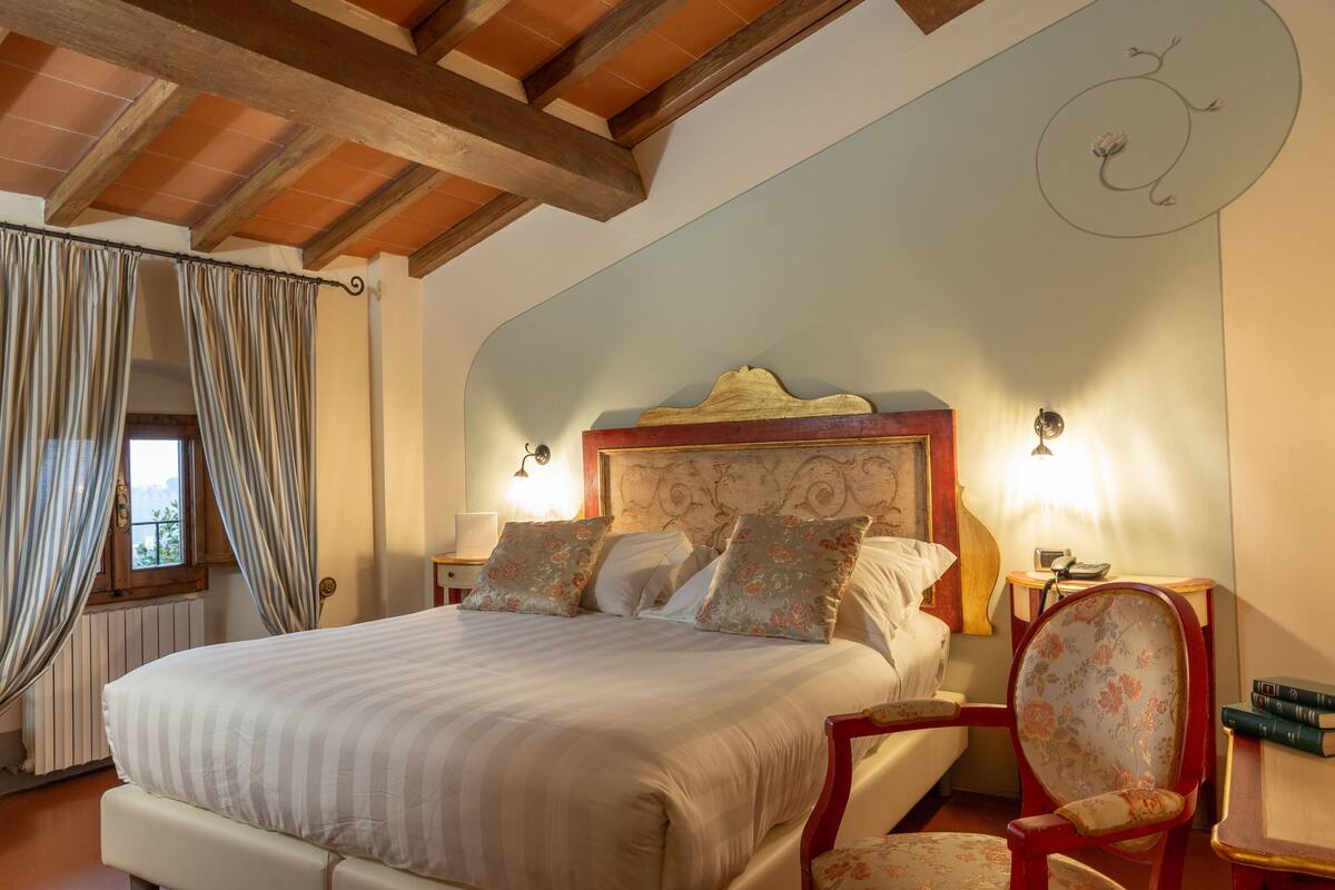 Une chambre à coucher avec un grand lit, une tête de lit en bois, deux tables de chevet avec des lampes, une chaise et une fenêtre avec des rideaux.