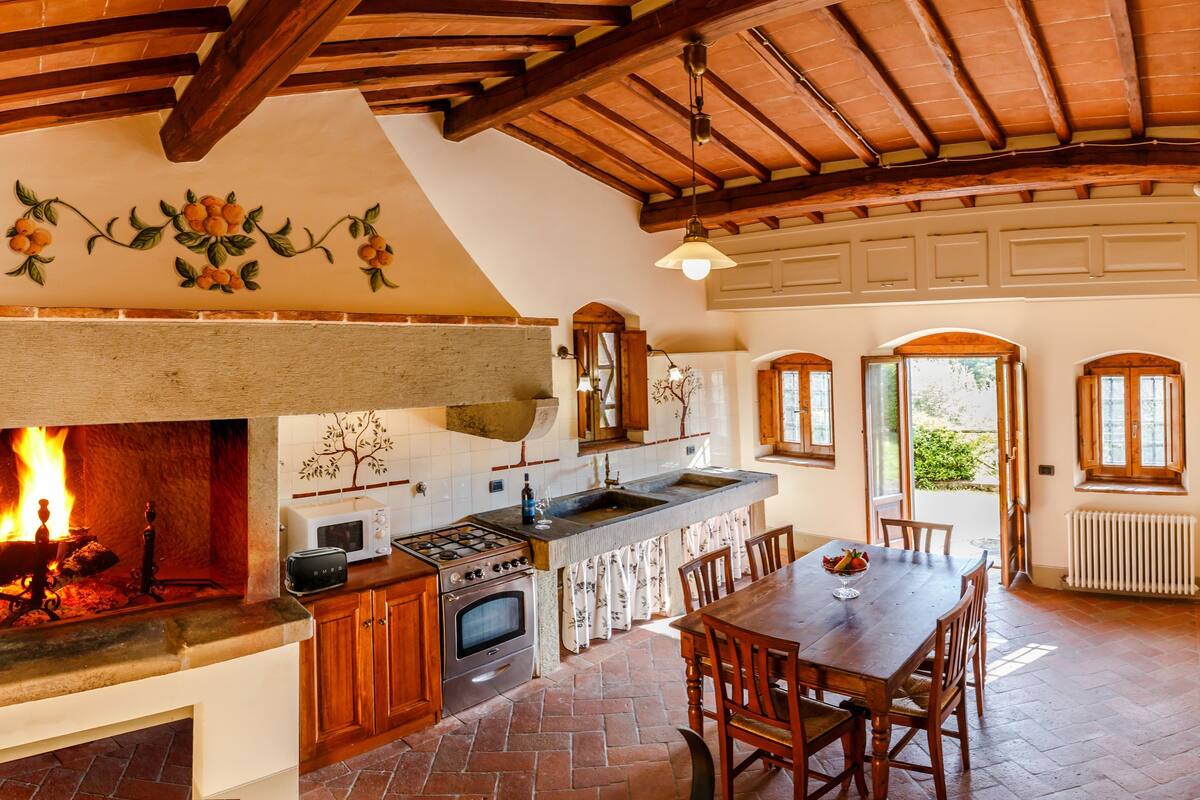 Una cocina rústica con chimenea, vigas de madera y un comedor con mesa y sillas.