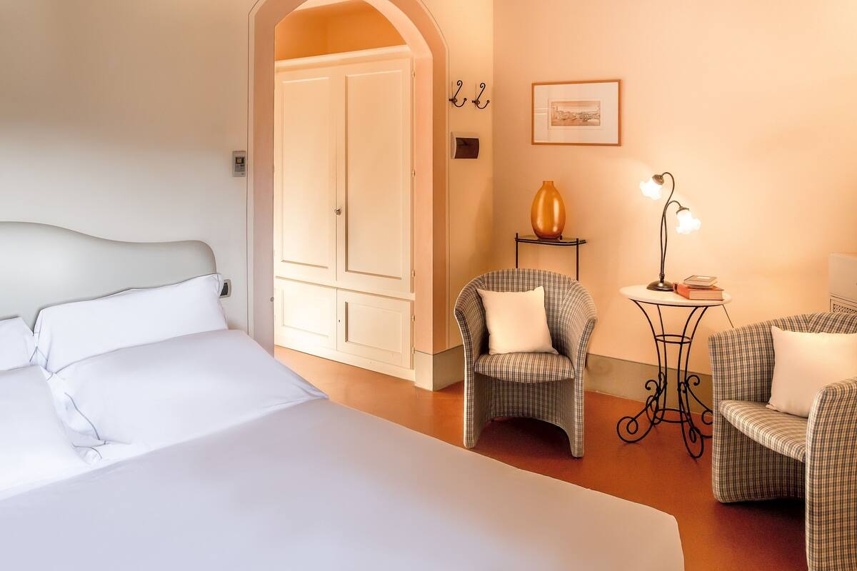Una habitación de hotel con una cama grande, una silla, una mesita y una lámpara.