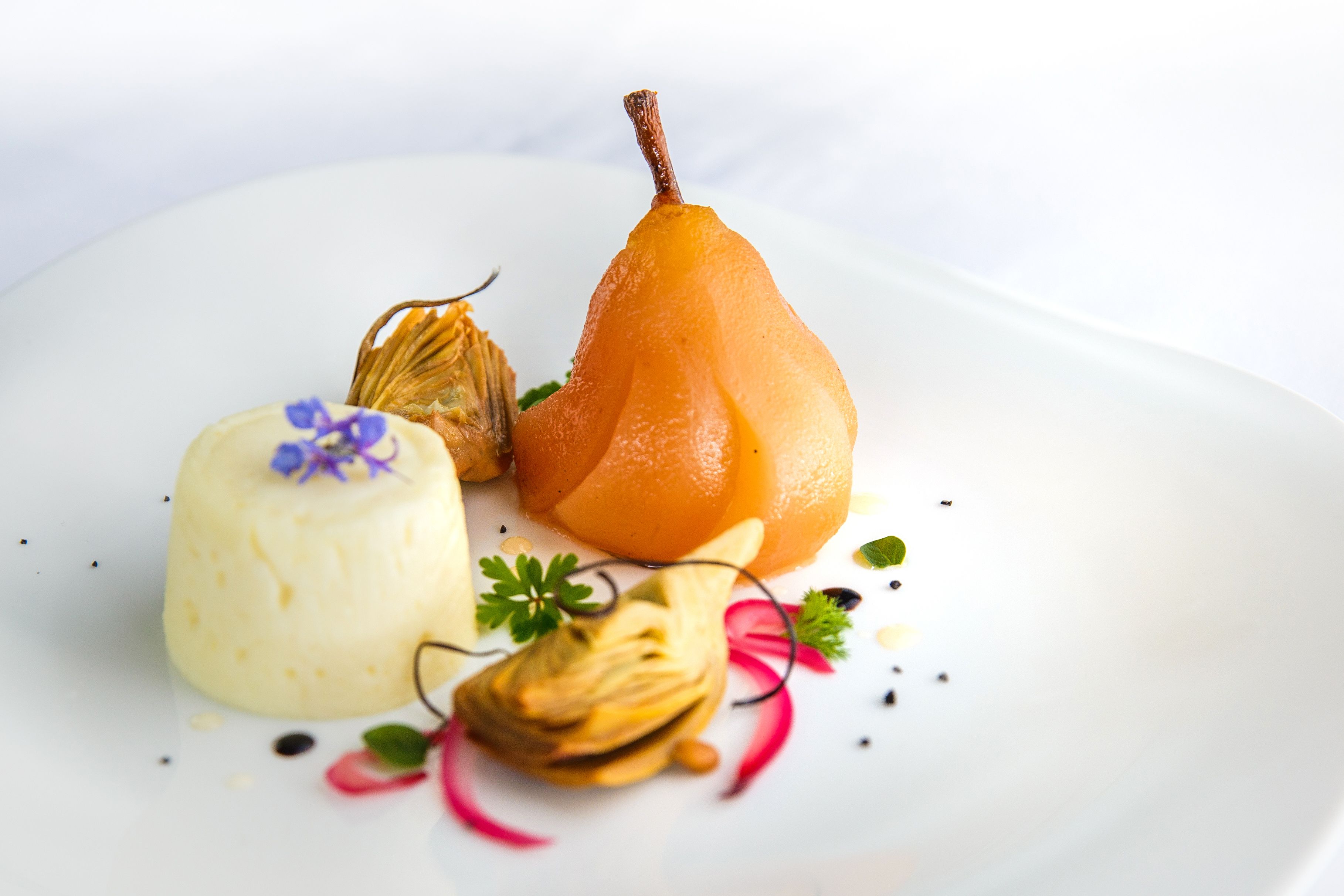 Un plato blanco con una pera, un objeto redondo y blanco, y un alcachofa.