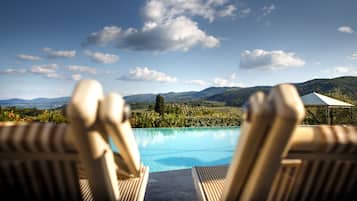 Une vue sur la piscine, avec des chaises longues, un ciel dégagé et un paysage montagneux en arrière-plan.