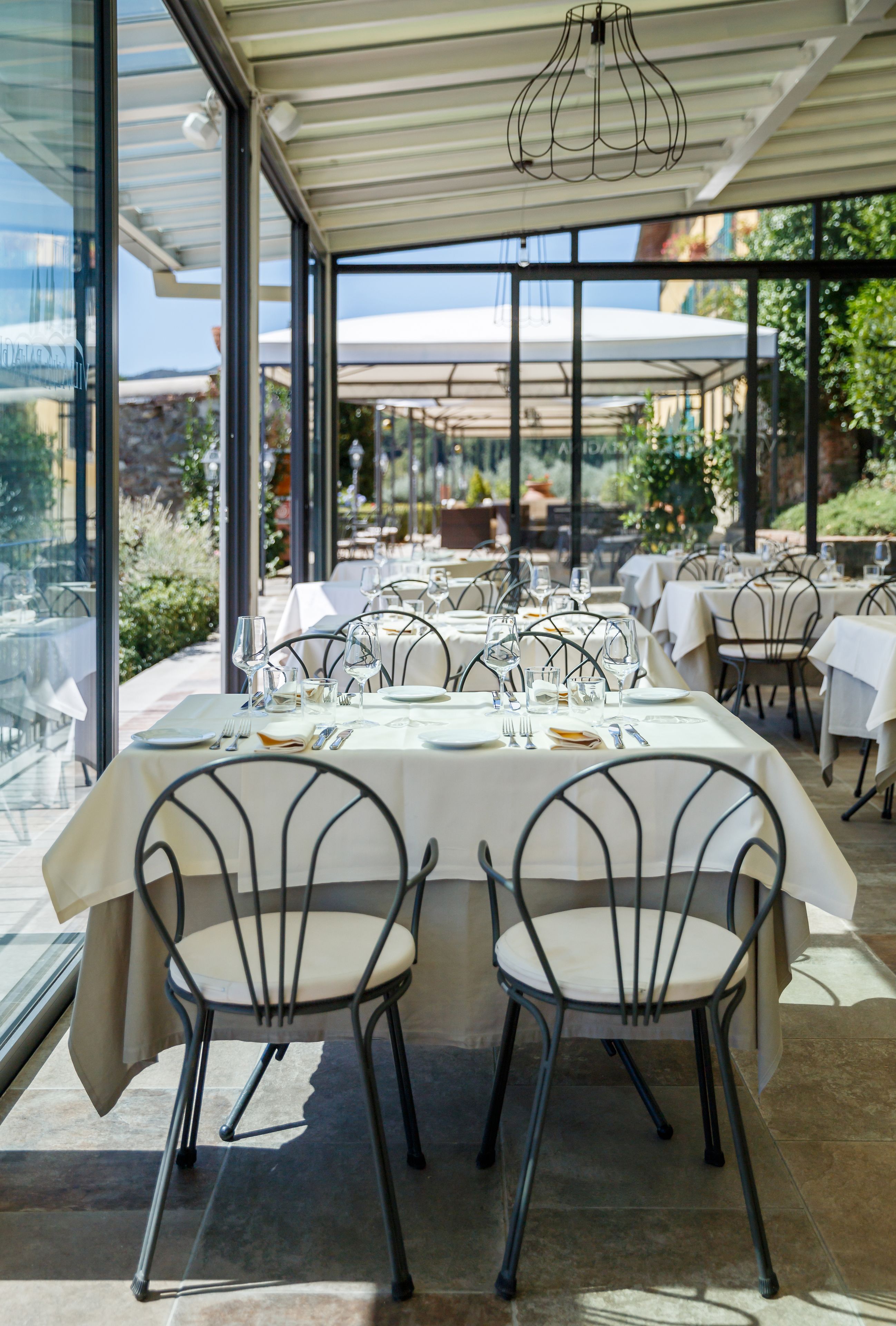 A restaurant with outdoor seating, tables set with white tablecloths, and metal chairs.