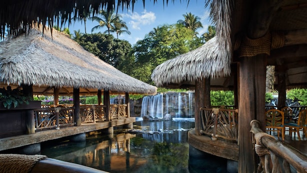 Resort com estruturas de telhado de palha, piscina com cachoeira e grades de madeira.