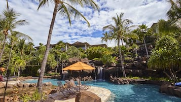A pool area with lounge chairs, a waterfall, and palm trees.