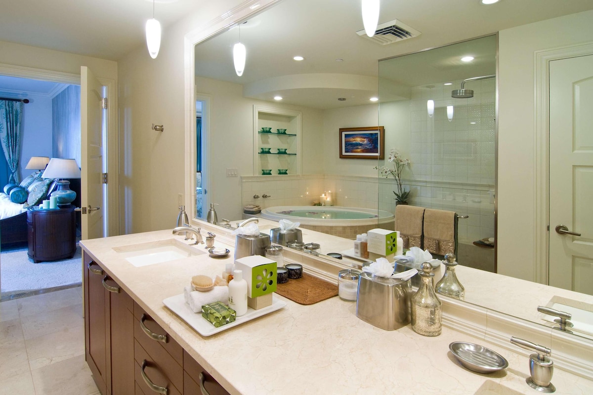 Une salle de bain moderne avec un grand miroir, une baignoire et une douche. On peut y voir divers produits de toilette et un porte-serviettes.