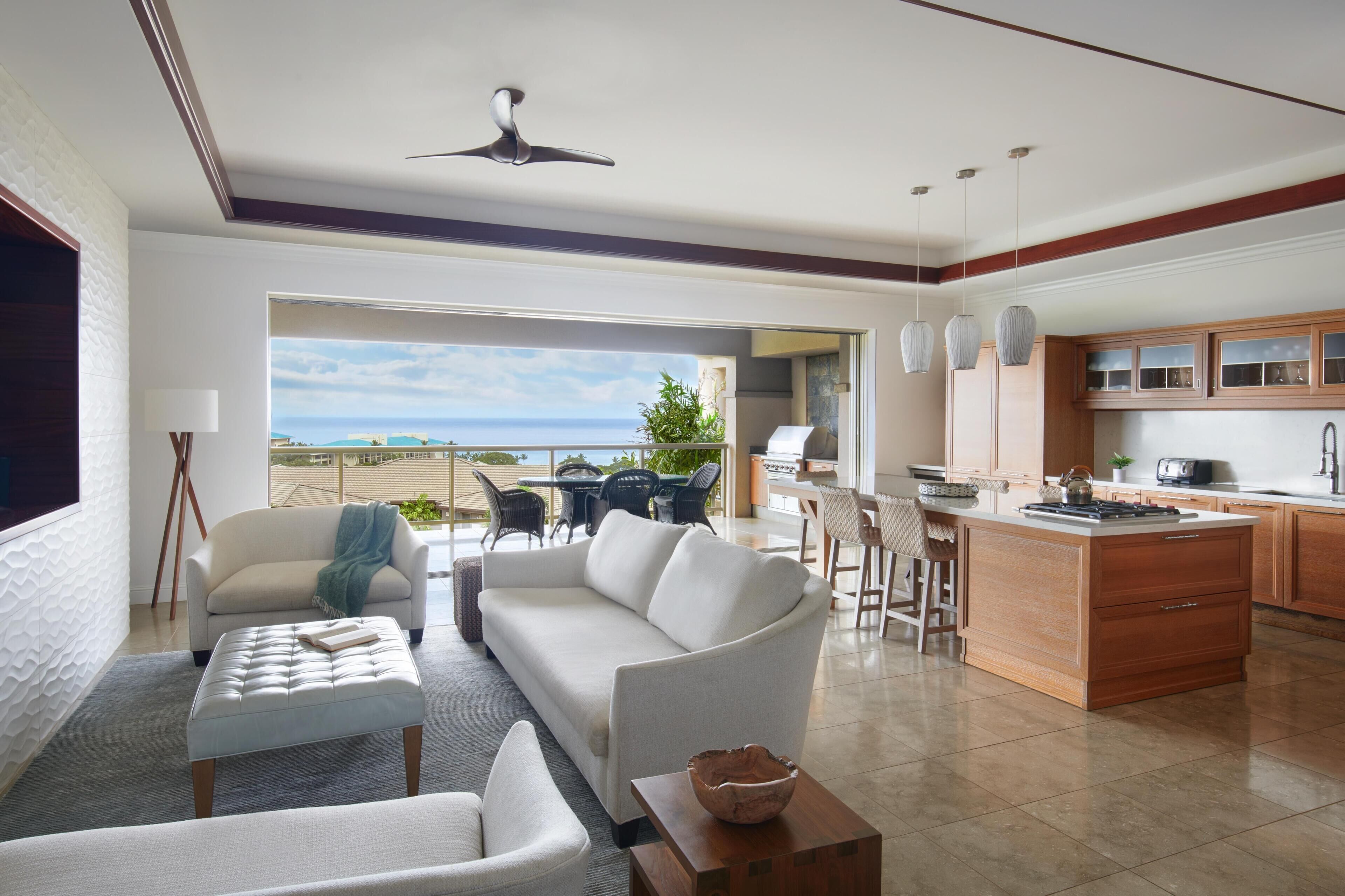 A modern living room with a sofa, ottoman, and coffee table, a kitchen with wooden cabinets, and a dining area with chairs.