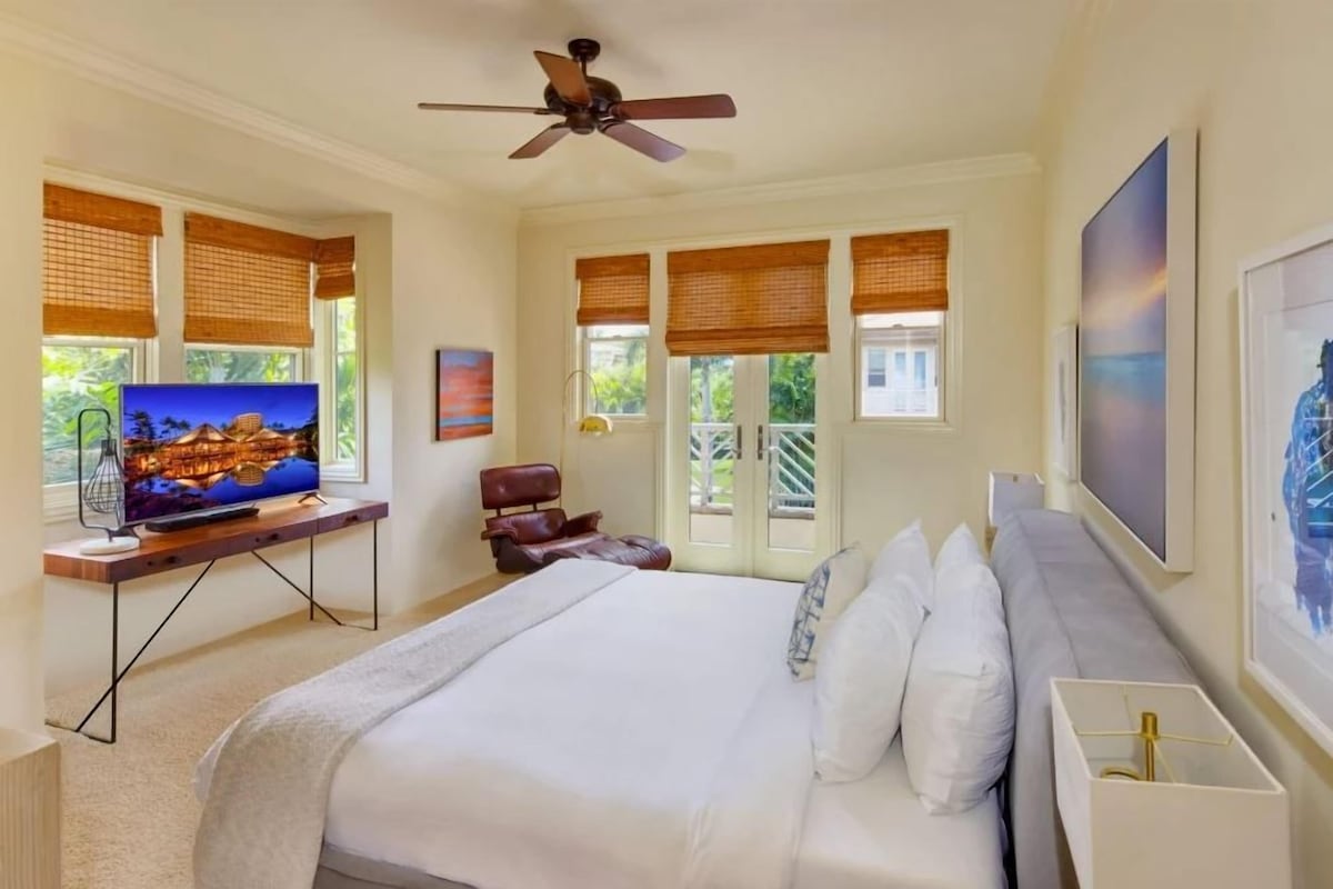 A bedroom with a bed, a TV, a ceiling fan, and windows with blinds.