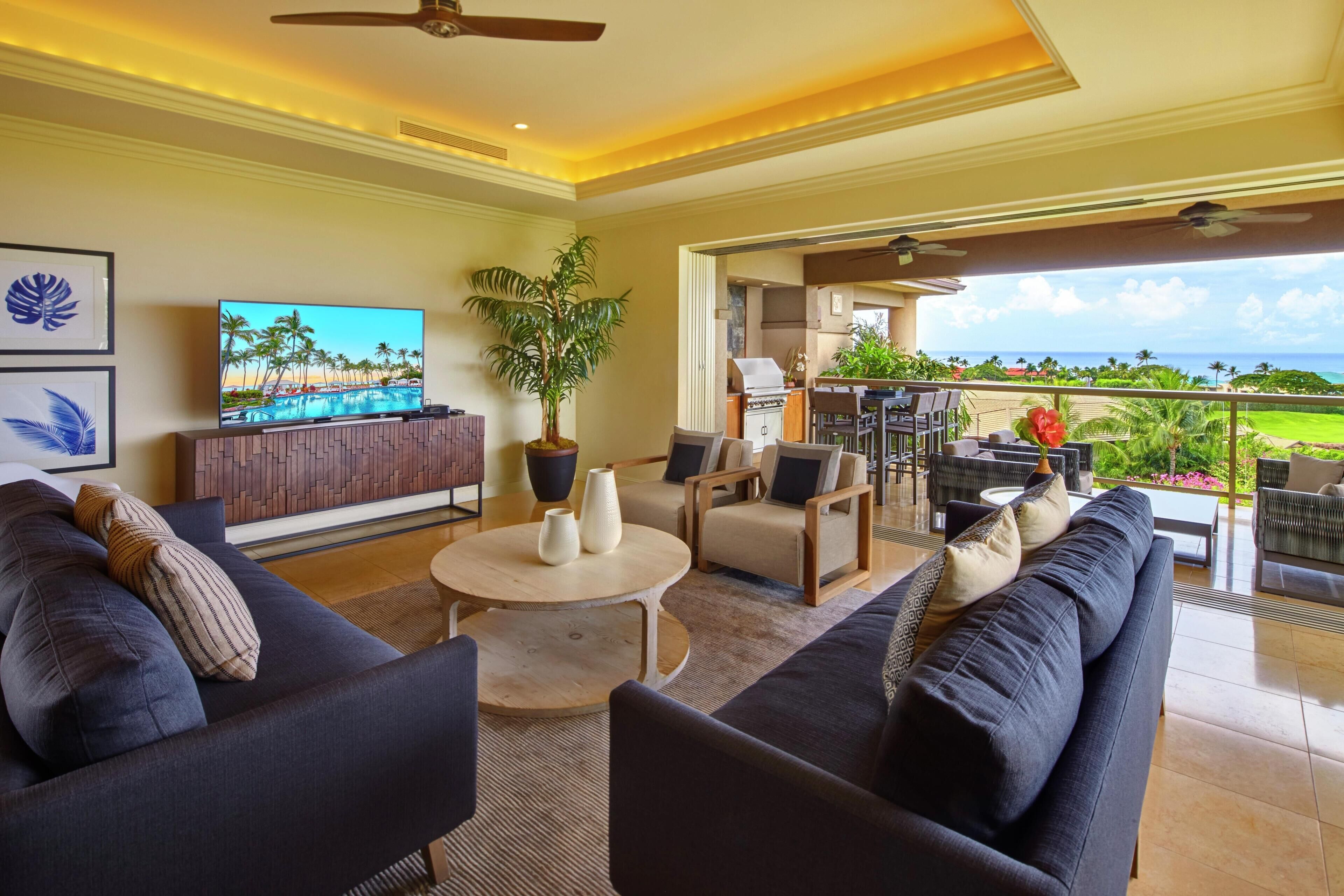A spacious living area with a TV, comfortable seating, a dining area, and a balcony with a view.