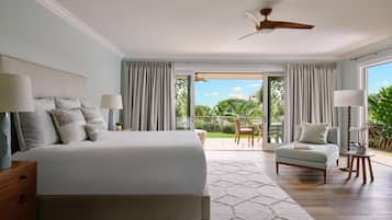 A bedroom with a large bed, a ceiling fan, a view of the outdoors, and a small seating area.
