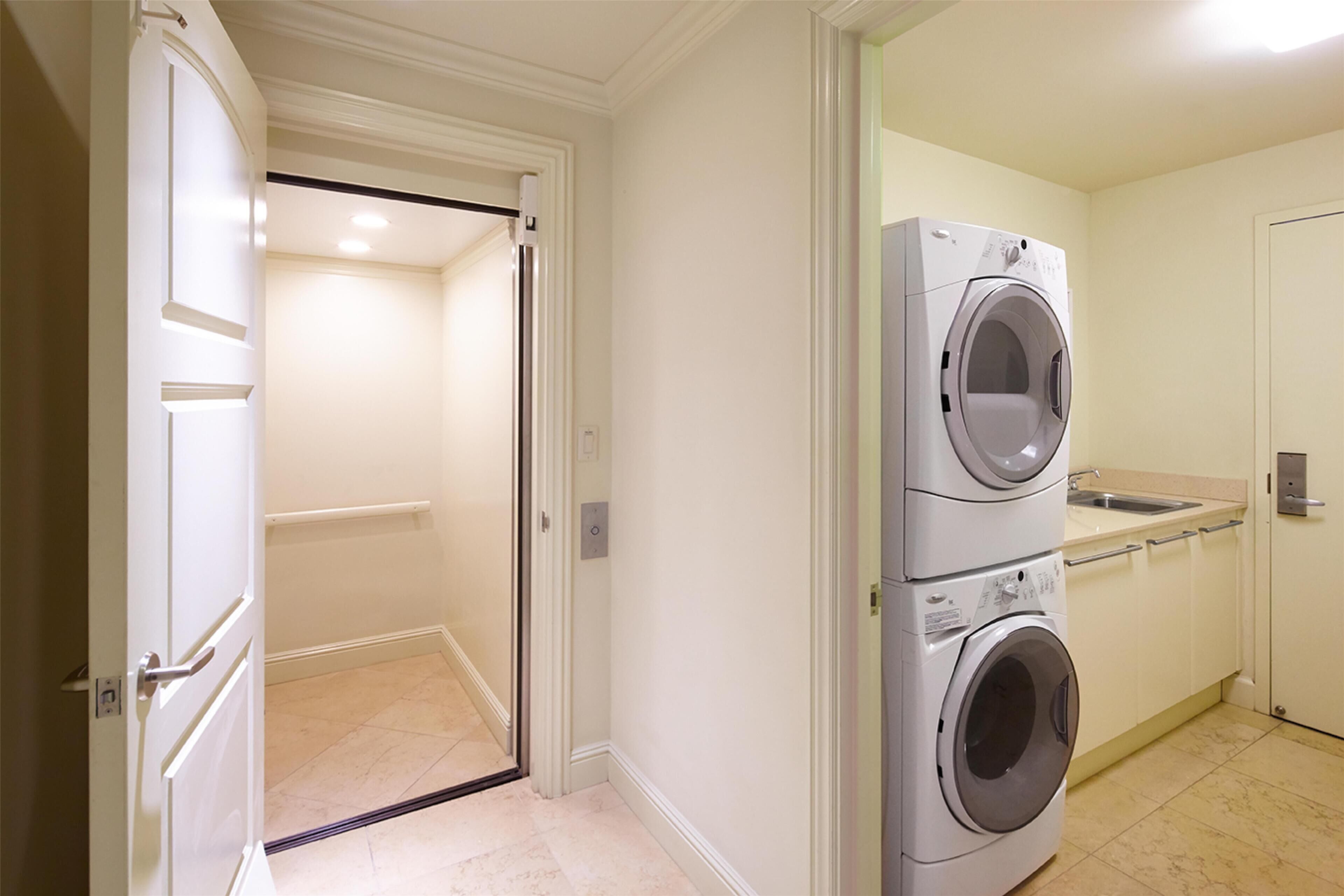 Un espace buanderie comprenant un lave-linge et un évier, une porte donnant sur un couloir, et un interrupteur sur le mur.