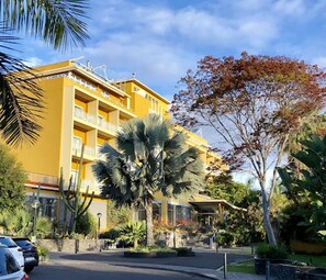 A yellow multi-story building with balconies, surrounded by palm trees and other vegetation. - Hotel Tigaiga (Puerto de la Cruz)