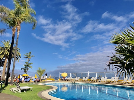 Una piscina al aire libre, sombrillas, sillones reclinables de piscina