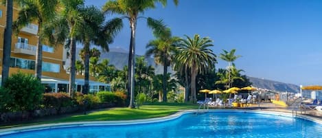 Una piscina amb palmeres i un edifici al fons.