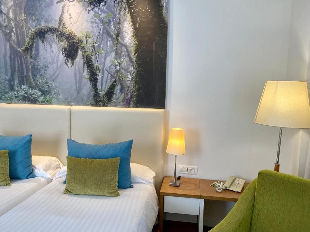Een hotelkamer met twee bedden, een nachtkastje met een lamp, een telefoon en een stoel.