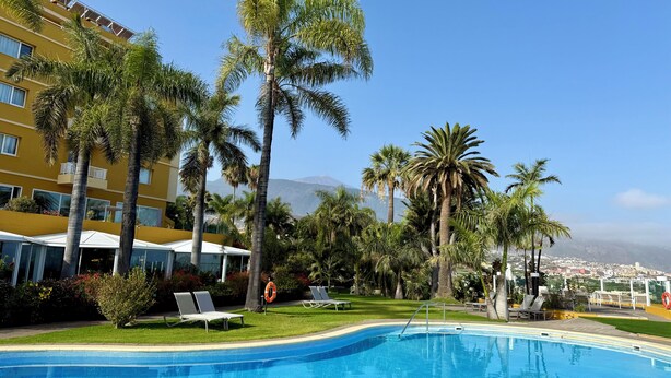 Ein Hotelpool mit Palmen, einem Rettungsring und einem Berg im Hintergrund.