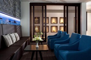 Un espace détente moderne avec un canapé marron foncé, une petite table sur laquelle est posé un vase de fleurs et des fauteuils bleus.