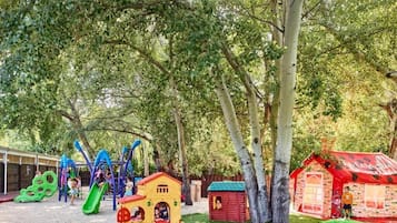 A playground with various play structures, including a slide and climbing frames, surrounded by trees.