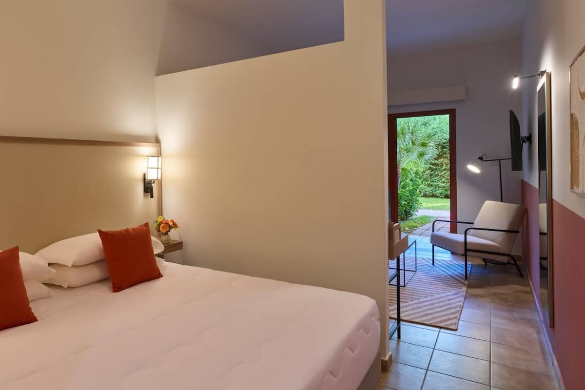 Ein Hotelzimmer mit einem großen Bett, einem Nachttisch mit Lampe und Blick auf den Garten.