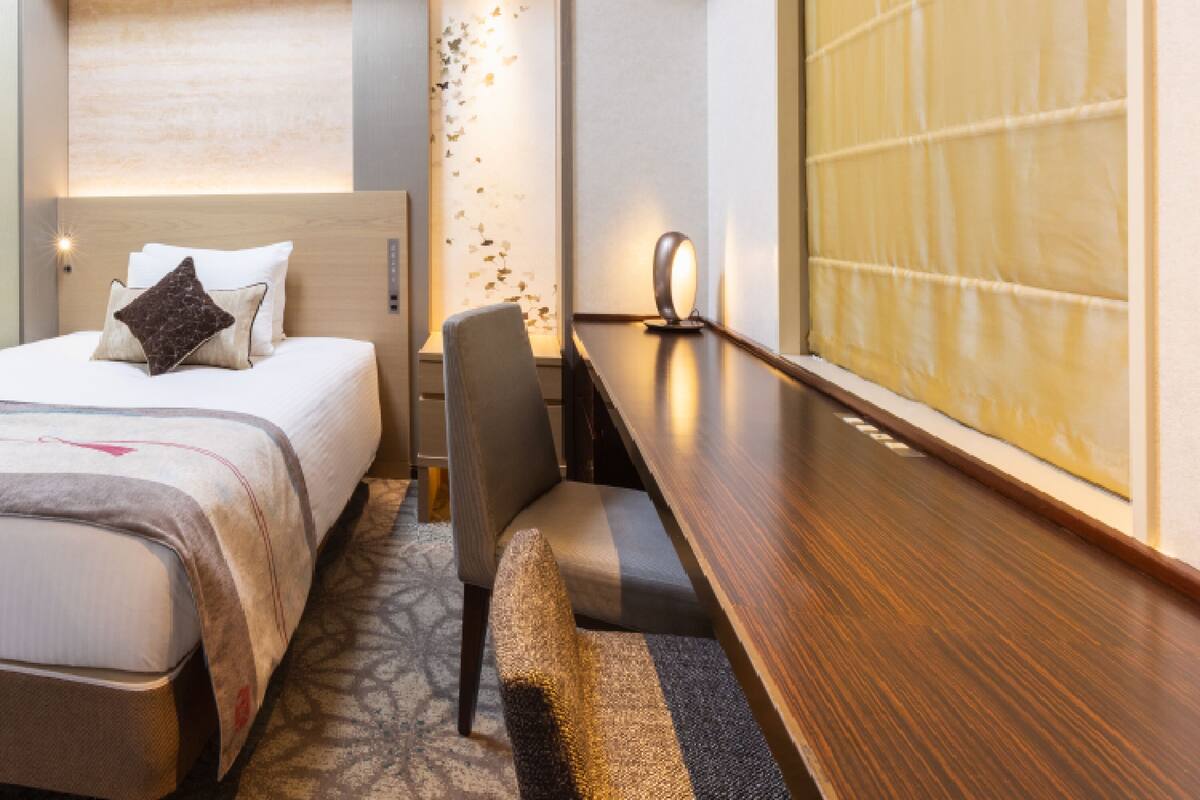 A hotel room with a bed, a desk, a chair, and a large window.