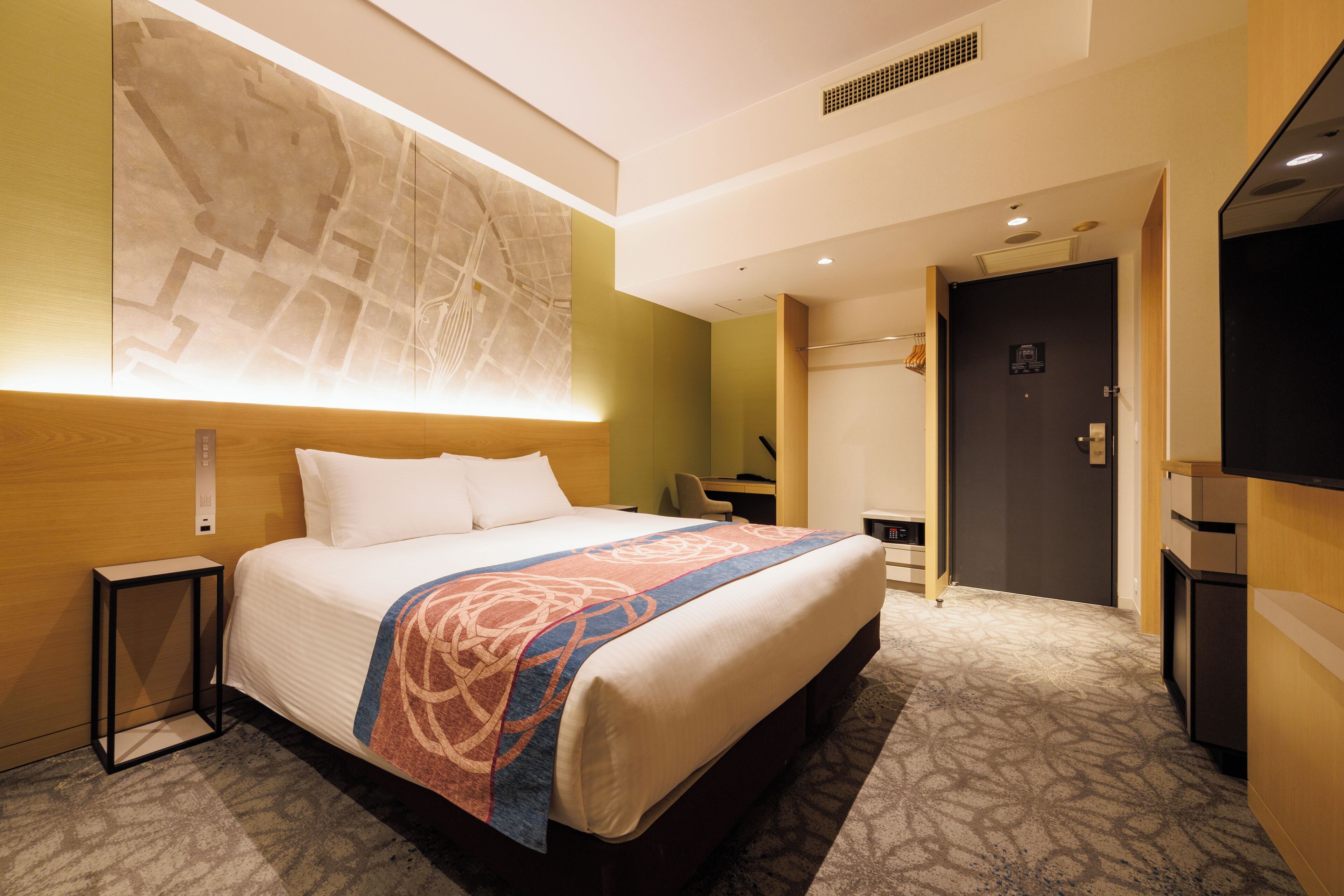 A hotel room with a large bed, a map on the wall, a desk, and a TV.