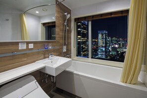 A modern bathroom with a sink, mirror, and shower. A cityscape is visible through a window.